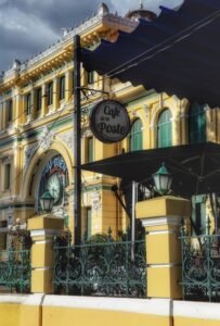 Yellow French colonial building with Café de la Poste sign and ornate iron fence.